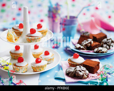 Fairy cakes, brownies au chocolat et chocolat crinkle cookies organisé sur un cakestand, sur des serviettes et des assiettes, tasses et pailles en arrière-plan Banque D'Images