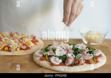 Ajouter le fromage râpé, jambon et champignons, pizza au thon et maïs doux pizza en arrière-plan Banque D'Images