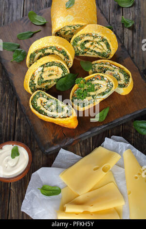 Roulade oeufs délicieux avec un remplissage de mélange d'épinards, la feta et les carottes coupées en tranches sur les planches à découper en bois avec la sauce et du fromage à foregro Banque D'Images