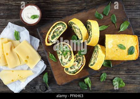 Roulade oeufs délicieux avec un remplissage de mélange d'épinards, la feta et les carottes coupées en tranches sur les planches à découper en bois avec la sauce et le fromage sur la table, Banque D'Images