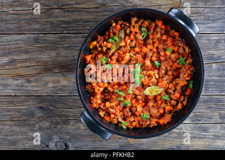 Ragoût délicieux avec les viandes hachées, les légumes et les tomates dans une casserole noire - ingrédient pour les pâtes à la bolognaise ou le pâté chinois, vue d'en haut Banque D'Images