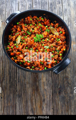 Délicieux ragoût classique avec la viande hachée, les légumes, les pois verts et les tomates dans une casserole noire - ingrédient pour les pâtes à la bolognaise ou le pâté chinois, ve Banque D'Images