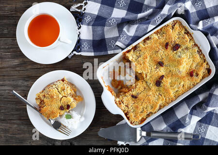 Crumble aux pommes savoureuses ou apple crisp dans le plat de cuisson et d'une partie sur la plaque avec une boule de glace au lait de coco. tasse de thé à l'arrière-plan, vue depuis un Banque D'Images