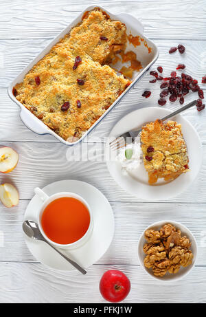 Jeu de petit-déjeuner sans gluten - crumble aux pommes ou apple crisp dans le plat de cuisson et d'une partie sur la plaque avec la crème de coco et une tasse de thé sur la table, vertical Banque D'Images