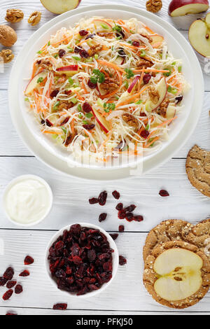 Close-up de pommes Canneberges et noix et salade de chou sur une assiette blanche sur table en bois avec des tranches de pomme rouge, multigrains pain croustillant, sauce yogourt et Banque D'Images