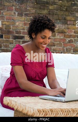 Femme enceinte à l'aide d'un ordinateur portable, assis sur le patio, close-up Banque D'Images