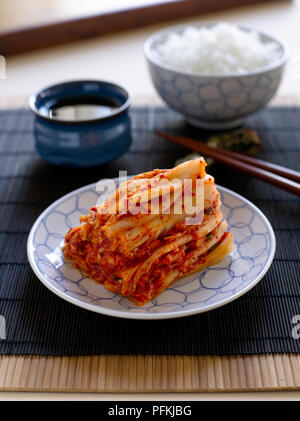 Baechoo le kimchi, chou chinois farci aux légumes, servi avec bol de riz blanc et la sauce de soja, bambou sur place mat Banque D'Images