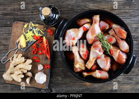 Pilons de poulet cru mariné à la sauce teriyaki épicé fait maison en noir pot. Ingrédients sur planche à découper en bois sur la table en bois, vue horizontale Banque D'Images