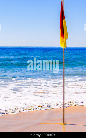 Le rouge et jaune beach flag sur une plage Banque D'Images