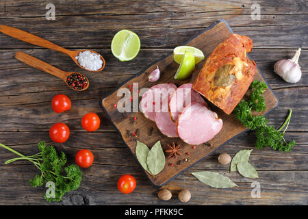 Délicieux jambon fumé coupé en tranches avec des épices, du persil et de la chaux sur planche à découper en bois foncé sur la vieille table en bois, vue du dessus Banque D'Images