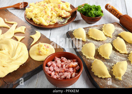 Les pierogi polonais traditionnels - ou l'Ukrainien dumpling. purée de pommes de terre, le jambon haché finement ou bacon dans des bols, pâte sur planche à découper en bois et ro Banque D'Images