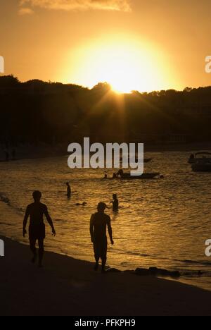 Antigua, Long Bay Beach, les gens dans l'eau et marcher le long de plage au coucher du soleil Banque D'Images