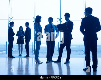 Silhouettes d'asian people standing parler affaires dans un bureau moderne. Banque D'Images