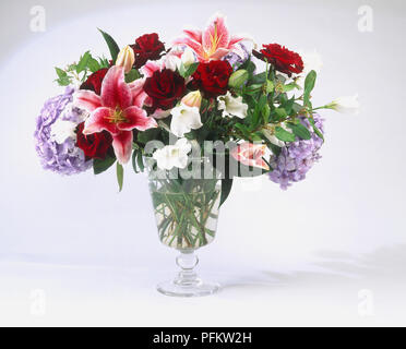 Un vase en verre contenant un gros bouquet de fleurs, notamment des roses, hortensias et nénuphars Banque D'Images