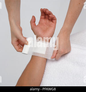 Woman's hands couvrant sur blessure au poignet du garçon avec bandage, close-up Banque D'Images