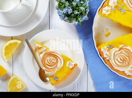 Morceau de tarte au citron classique français ou tarte au citron sur une assiette et dans un plat allant au four avec une crème anglaise remplissage citron meringue décoré de roses et d'e Banque D'Images