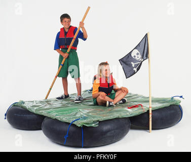 Boy and girl assis sur un radeau, drapeau pirate attaché à l'avant Banque D'Images