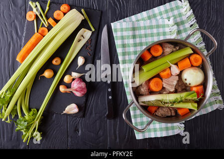 Ou blanquette de veau cuit - Morceaux de viande de veau en cocotte avec le bouquet garni et les légumes. des bâtonnets de céleri et l'ail sur la planche à découper noire wit Banque D'Images