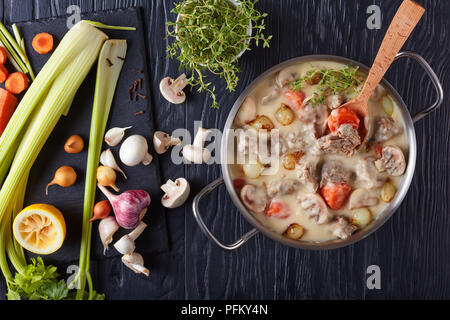 Ragoût de veau crémeux ou blanquette de veau - morceaux de ragoût de veau aux champignons, petits oignons glacés, des herbes et des légumes dans une casserole sur noir woode Banque D'Images