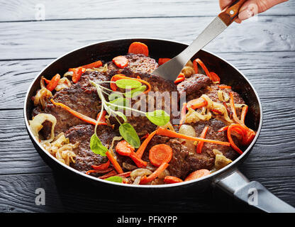 Foie de poulet crêpes avec carotte, oignon, épices et feuilles de sauge dans une poêle sur une table en bois noir, vue de dessus, close-up Banque D'Images