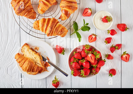 De délicieux croissants fraîchement cuits sur une grille et sur une plaque blanche avec des fraises mûres fraîches et crème, vue de dessus, close-up Banque D'Images