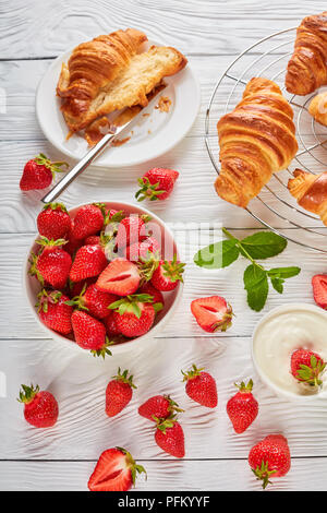 De délicieux croissants fraîchement cuits sur une grille et des bols d'une fraise mûre et de crème sure sur table en bois, vue verticale d'en haut Banque D'Images