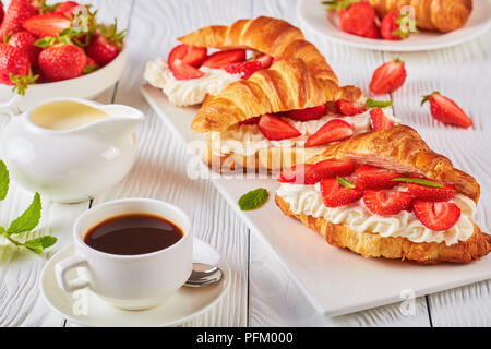 Petit-déjeuner d'été - un croissant frais mûrs sandwiches avec fraises et crème fouettée fromage sur un plateau. tasse de café, pot de crème fraîche et le bol Banque D'Images