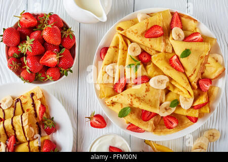 Crêpes minces ou des crêpes sur une plaque avec des fraises, des tranches de banane et de crème au chocolat, vue horizontale d'en haut Banque D'Images