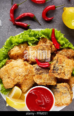 Morceaux de merlu frit sur une plaque blanche sur une table en béton avec des rondelles de citron, la sauce tomate et le piment, vue verticale d'en haut Banque D'Images