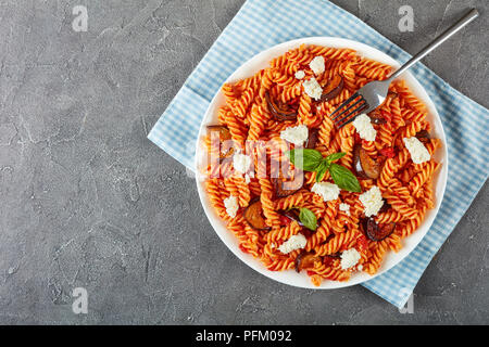 Les pâtes italiennes Les fusilli alla Norma avec des aubergines, tomates, basilic, de ricotta dans une assiette blanche avec silver fork sur une table, vue horizontale Banque D'Images