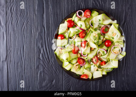 Courgettes délicieux salade de tomates avec du ruban, des cacahuètes grillées, oignons rouges et verts sur une plaque noire sur une table en bois, de style méditerranéen, en bonne santé Banque D'Images