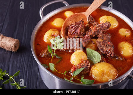 Un délicieux ragoût de boeuf pot avec de tendres cubes de viande, tout nouveau les pommes de terre, les carottes et les herbes dans un chaudron sur une table en bois noir avec bouquet de l'aaa Banque D'Images
