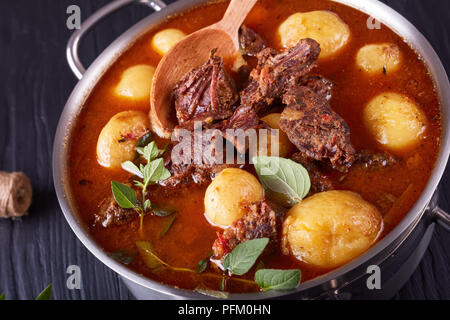 Ragoût de boeuf chaud avec de tendres cubes de viande, tout nouveau les pommes de terre, les carottes et les herbes dans un chaudron sur une table en bois noir avec bouquet d'herbes aromatiques, vi Banque D'Images