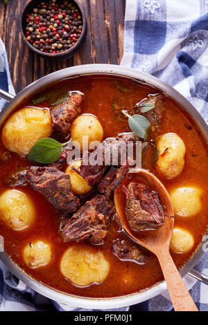Ragoût de boeuf avec des cubes de viande tendre, ensemble de nouvelles pommes de terre, les carottes et les herbes dans une casserole de métal sur la vieille table en bois rustique avec des essuie-tout, des Irlandais c Banque D'Images