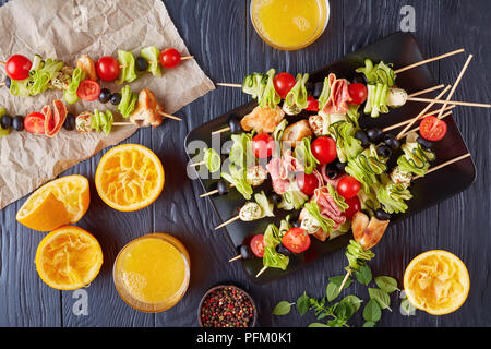 L'antipasto brochettes avec la viande de poulet, courgettes, tomates cerises crus, boules de mozzarella, salami en tranches, les olives sur une plaque sur une table en bois avec orange Banque D'Images