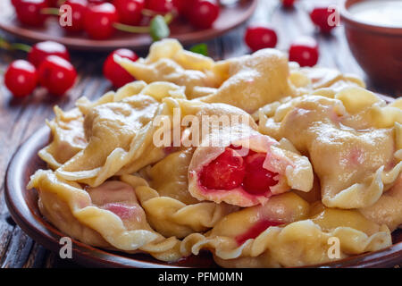 Délicieux chaud boulettes cerise sur une plaque d'argile sur une table en bois. une plaque avec des cerises fraîches et le bol avec de la crème sur une table rustique, vue depuis l'ab Banque D'Images