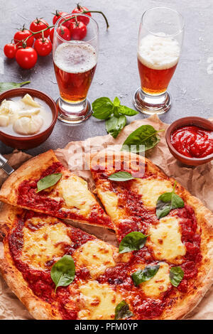 Classic Italian Pizza Margherita sur un papier parchemin sur une table en béton avec de la bière dans des tasses en verre, vertical Vue de dessus Banque D'Images