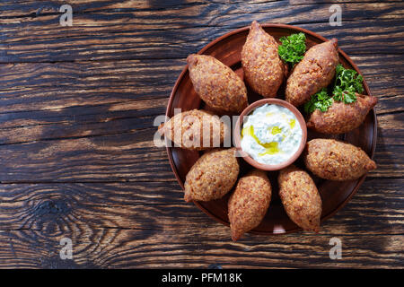 Frit délicieux avec du yaourt kibbeh sauce dans un bol servi sur une plaque d'argile sur une vieille table en bois foncé, recette classique, vue de dessus, copiez l'espace, fl Banque D'Images