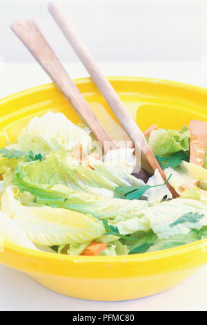 Salade verte dans un bol en plastique jaune avec fourches en bois servant, Close up Banque D'Images