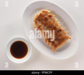 Gyoza, huit de style chinois frits boulettes, servi sur assiette blanche, à côté de bol de sauce soja, vue de dessus. Banque D'Images