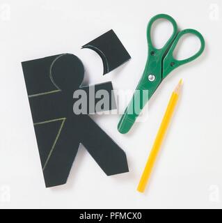 Plan d'une personne coupé d'un morceau de carton noir, ciseaux et crayons de couleur à proximité Banque D'Images