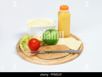 Bouteille de jus d'orange frais, à remous de la margarine, pomme, tomate, laitue, feuilles de farine complète pain pitta, fromage et couteau sur planche à découper Banque D'Images
