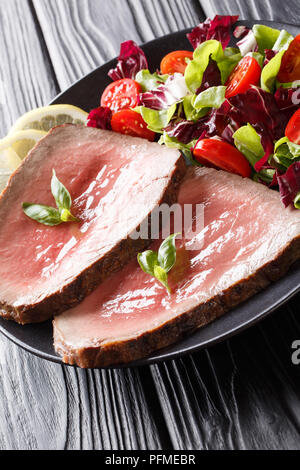 Rares fraîchement cuit steak de boeuf avec une salade de légumes frais close-up sur une plaque sur une table verticale. Banque D'Images