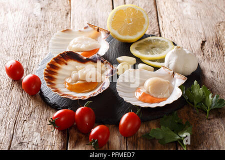 Délicieux pétoncles crus dans un shell et les tomates, ail, persil et citron gros plan sur une table de bois horizontal arrière-plan alimentaire. Banque D'Images