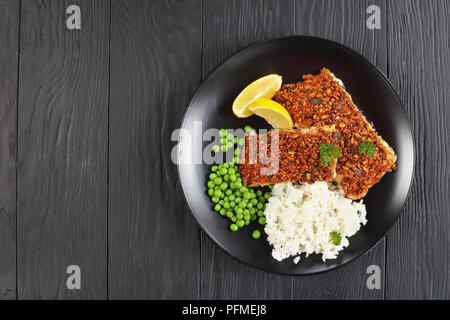 Citrouille, graines de tournesol et de Chili Filets de poisson en croûte servi avec du riz et des pois verts sur la plaque noire, vue d'en haut Banque D'Images