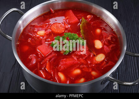 Close-up of delicious soupe rouge de betterave avec le haricot blanc ou bortsch dans une casserole en acier inoxydable pan sur table en bois noir, recette authentique, horizon Banque D'Images