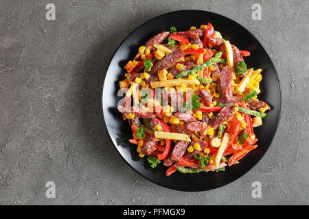 Délicieux fromages, saucisses, d'asperges cuites à la vapeur, le maïs et salade de poivron rouge parsemé de croûtons sur la plaque noire sur fond de béton, vue à partir de Banque D'Images