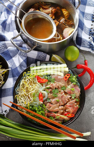 Délicieux soupe vietnamienne Pho Bo avec des faux filet de boeuf en tranches bol noir avec des baguettes d'os de bœuf chaud. bouillon dans l'acier inoxydable et autres ingredien pan Banque D'Images