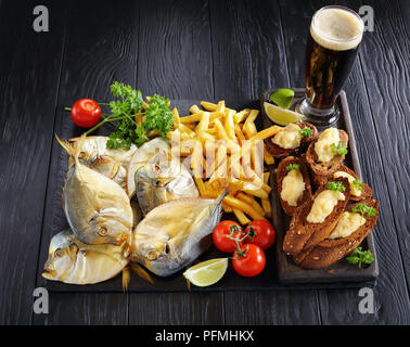 Délicieux poisson lune fumé à froid et frites servi sur un plateau avec pierre noire caviar capelin toasts croustillant et un verre de bière brune, mousse voir fr Banque D'Images