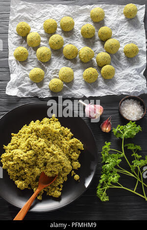 Boules de falafel brutes sur papier prêt à être frits. de pois chiches, la pâte fraîche persil, ail, sur table en bois noir, vertical Vue de dessus Banque D'Images